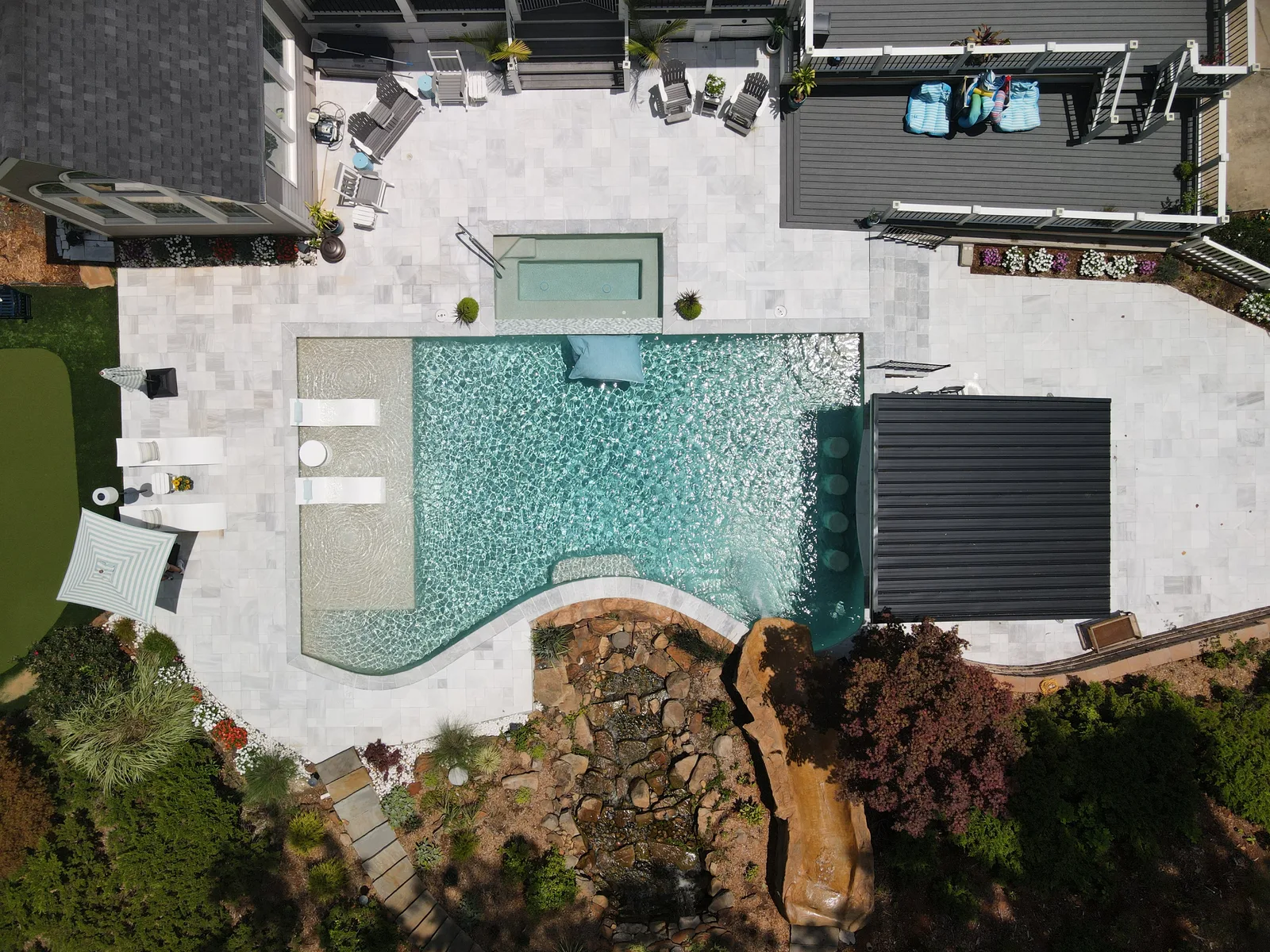 Drone view of a curved pool with a rock waterfall and green landscaping