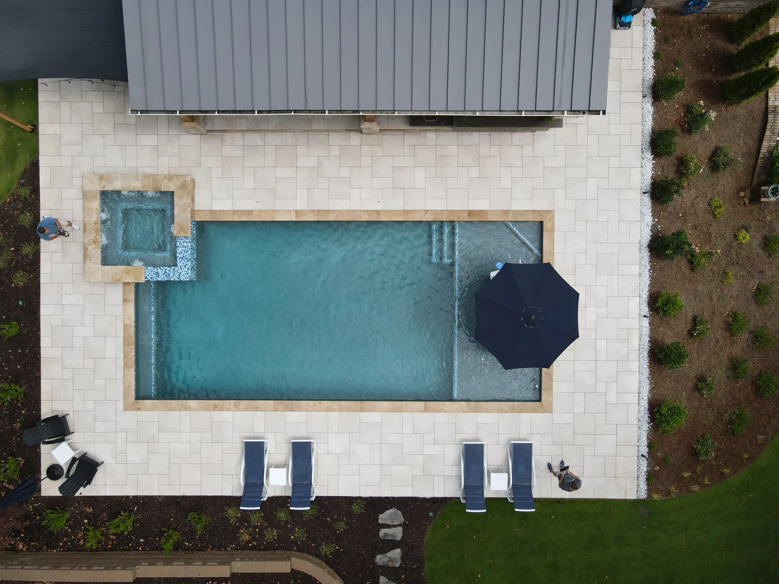 Drone view of a pool with lounge chairs and an umbrella on the patio